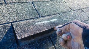 Homeowner inspecting worn shingles and moisture marks in a residential attic.