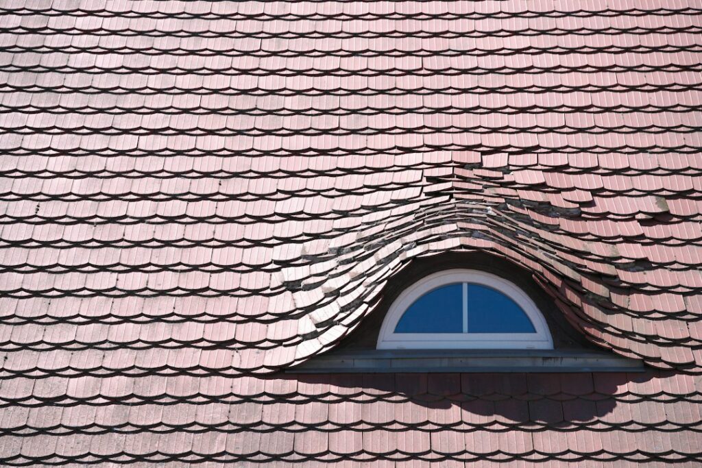 Inspector examining roof shingles and flashing beside a ladder while documenting visible wear.